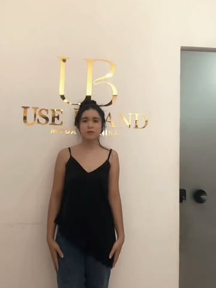 Modelo de blusa preta diante da parede com a logo dourada da Use Brand
